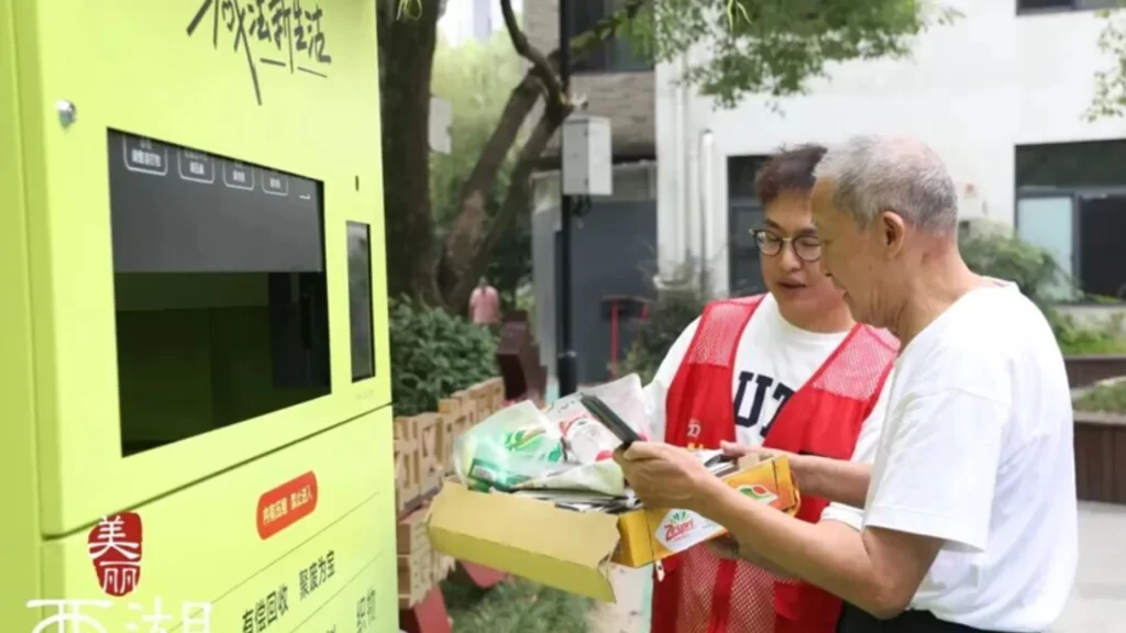 A volunteer helps a Hangzhou resident use a smart recycling station for digital waste management.