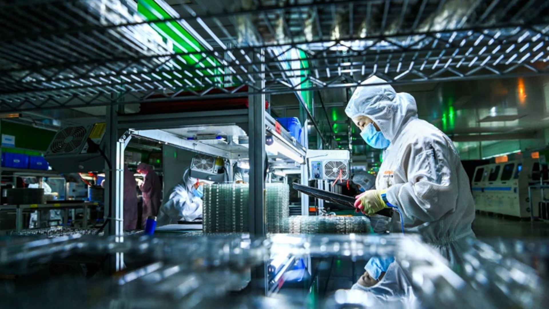 Workers in protective gear assemble high-tech components in a clean, modern Chinese manufacturing facility.