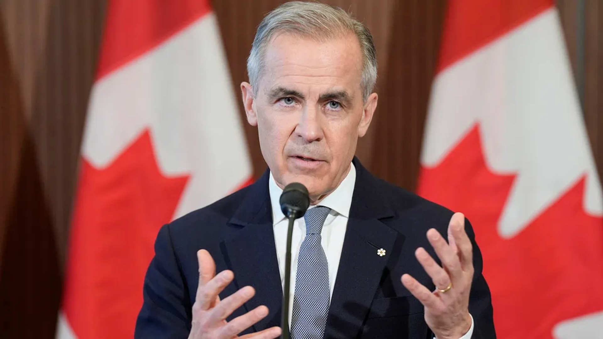 Canadian Prime Minister Mark Carney speaking at a podium with Canadian flags behind him.