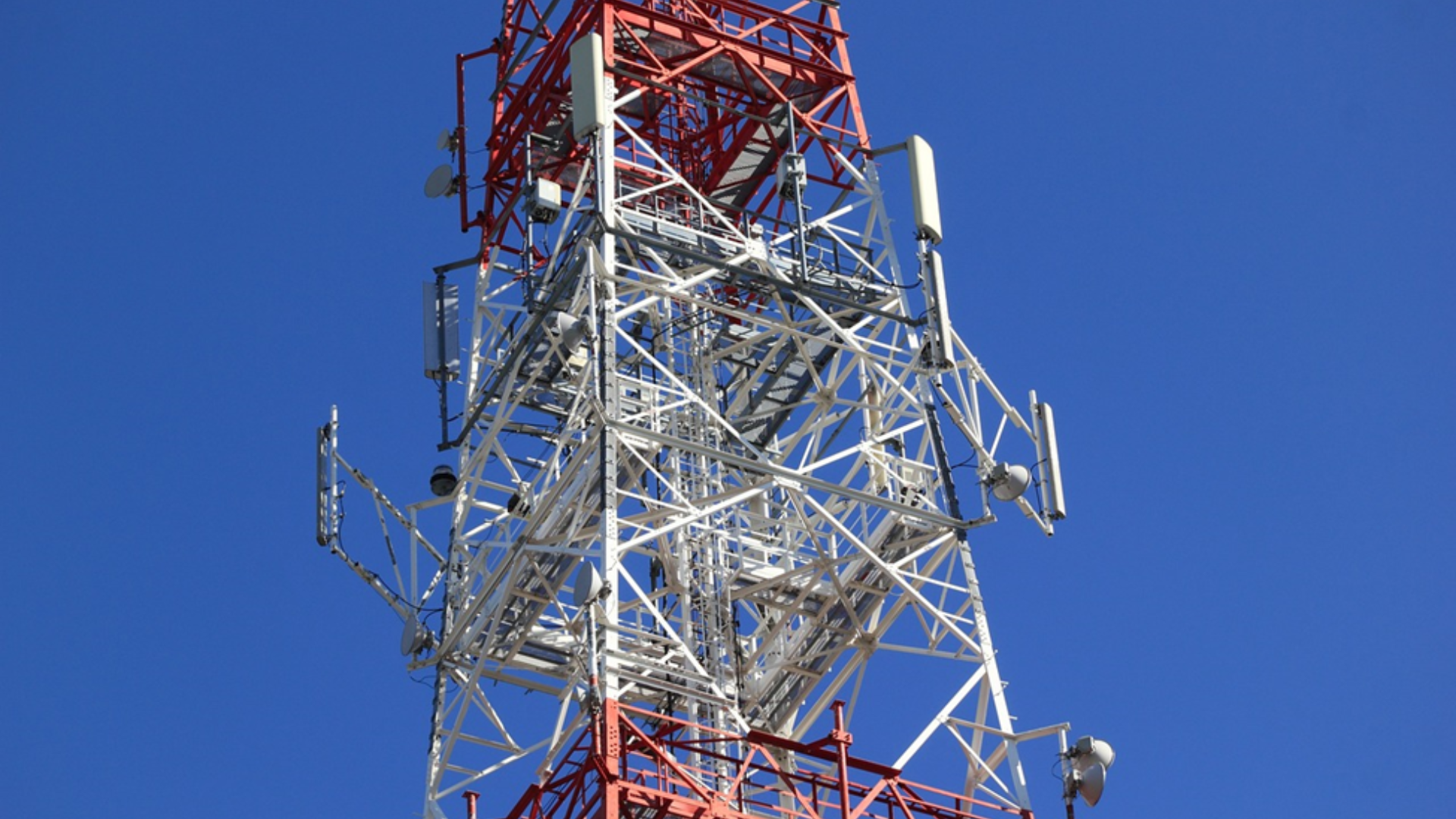 An orange and white telecommunications tower against a clear blue sky, illustrating Nigerian network infrastructure.