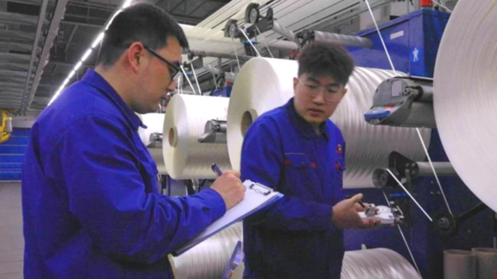 Two technicians inspect large spools of precursor during large-scale carbon fiber manufacturing in Jilin.