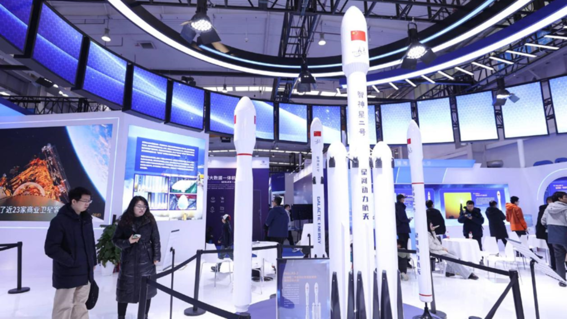 Visitors viewing models of Chinese commercial rockets at an indoor aerospace technology exhibition.