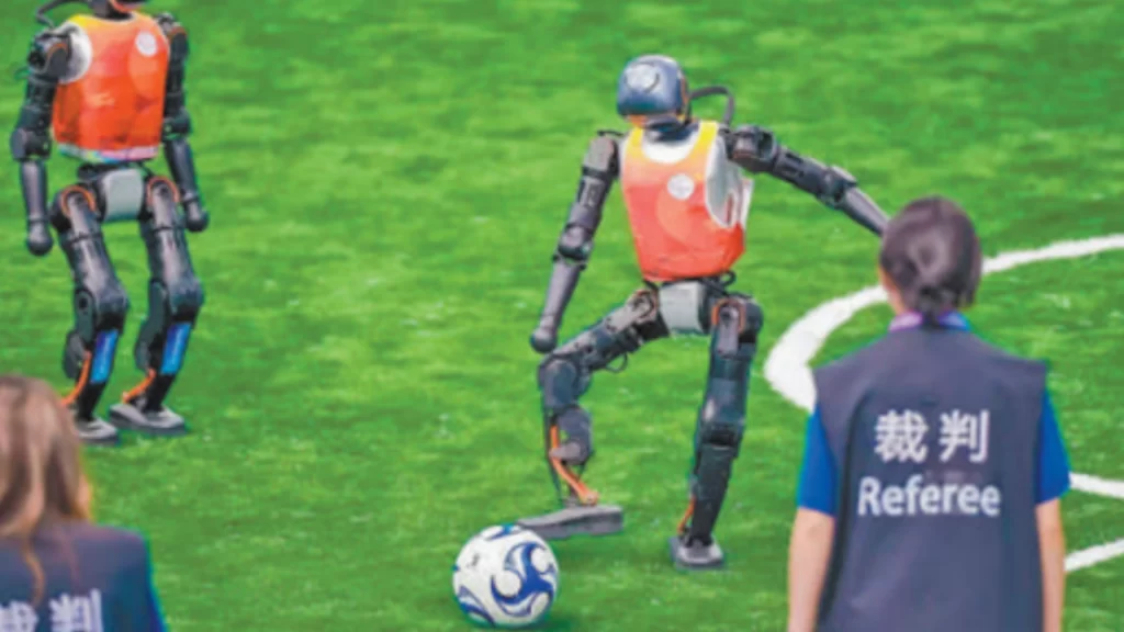 Two humanoid robots in orange jerseys play soccer on a green pitch before human referees.