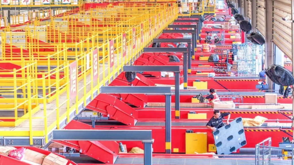 Workers managing goods along an automated conveyor line inside a large parcel sorting facility.