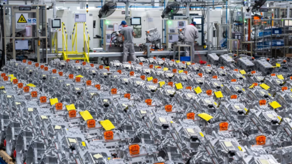Rows of manufactured automotive components fill a factory floor with workers at assembly stations.