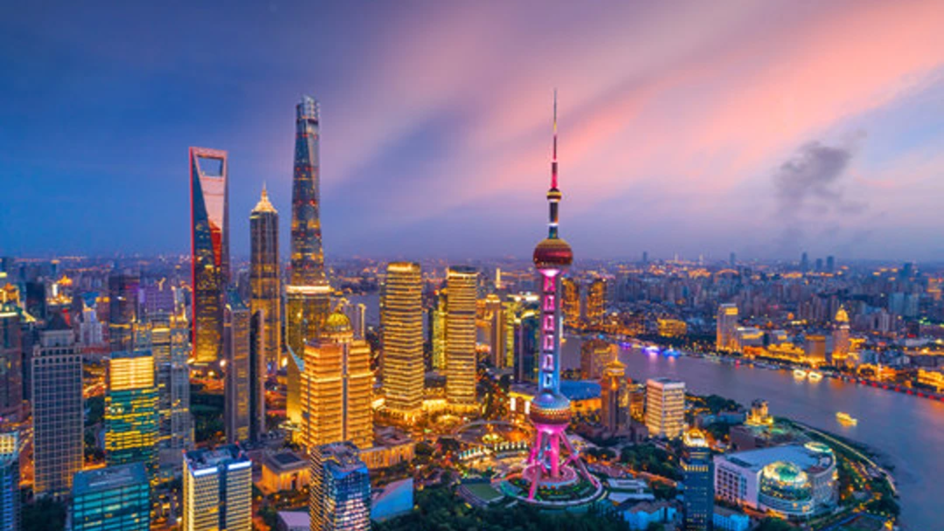 An aerial view of the illuminated Shanghai skyline and Oriental Pearl Tower at sunset.