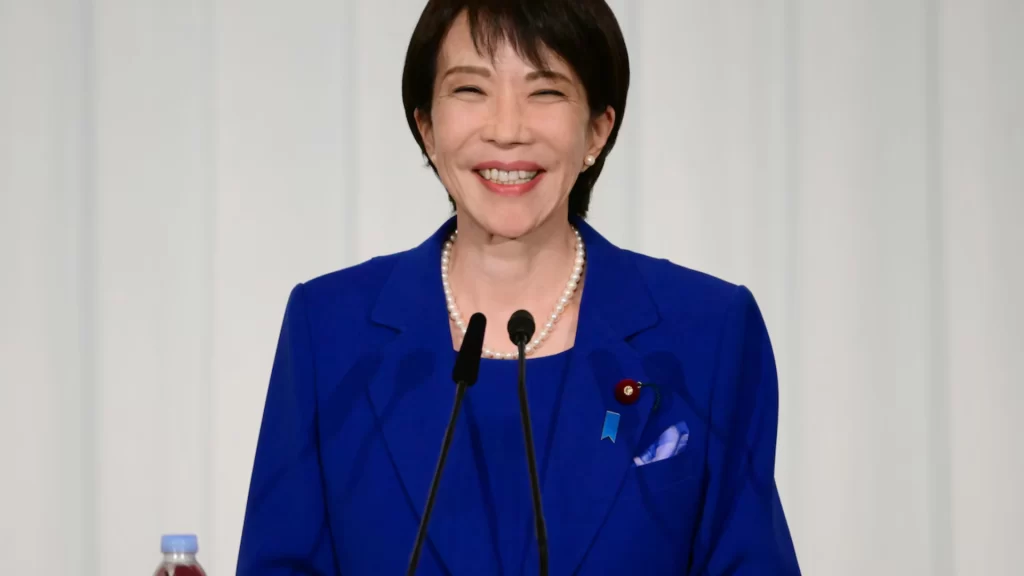 Japanese Prime Minister Sanae Takaichi smiling at a podium during a security press conference.