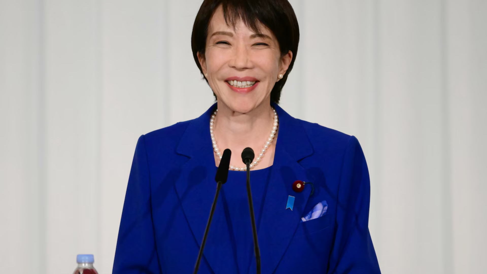 Japanese Prime Minister Sanae Takaichi smiling at a podium during a security press conference.