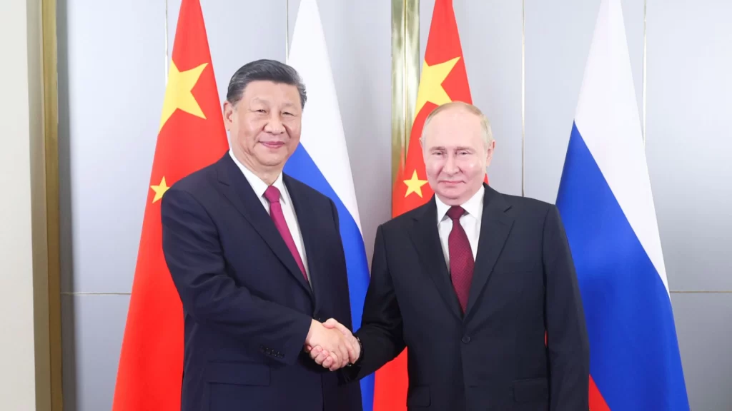 President Xi Jinping and President Vladimir Putin shake hands in front of national flags.