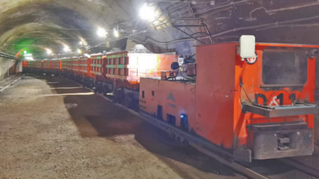 An orange 5G-powered autonomous ore train travels through an underground mine.