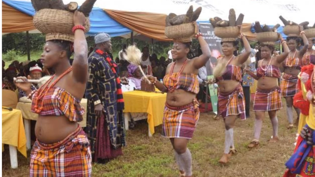 Igbo dancers in traditional attire carry baskets of newly harvested yams on their heads.